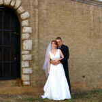 Bride and groom pose by brick wall