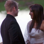 Bride and groom pose by water